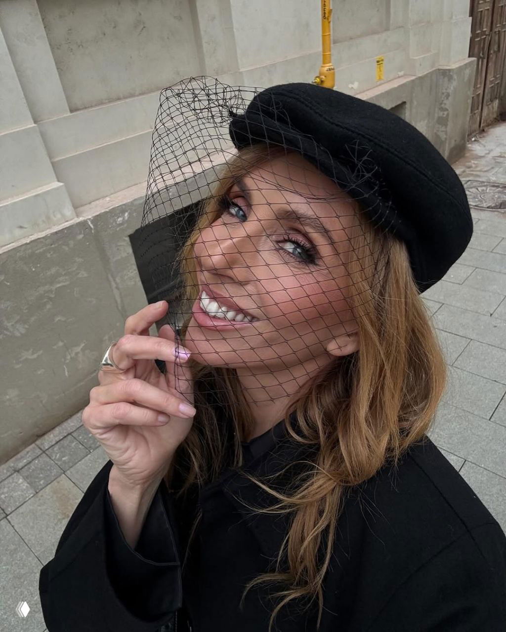 Крупный план: Светлана Бондарчук в черном берете с вуалью, мягкий макияж и улыбка на фоне городского фасада, тотал-блэк стиль.