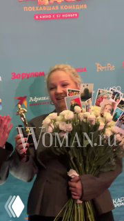 Варвара Щербакова улыбается, держит букет белых цветов и шуточную статуэтку «Оскар» на премьере «По‑братски».