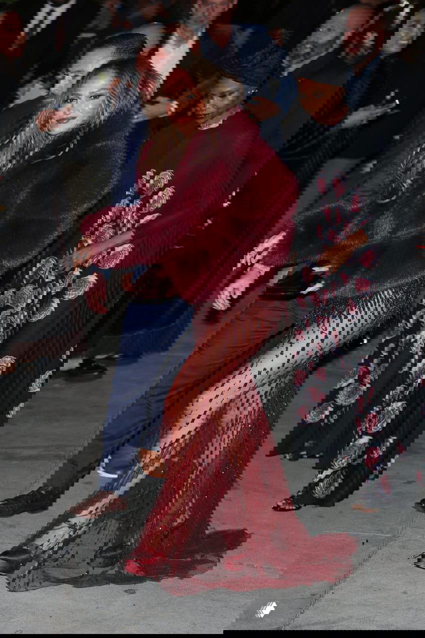 Дженнифер Лопес покидает мероприятие в составе группы сопровождающих, в бордовой шубе поверх кутюрного платья с кристаллами; кадр у входа