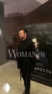 Мужчина в пальто на фоне постера фильма «Сущность» на премьере в кинотеатре «Октябрь», вечерний кадр с гостем у постера.