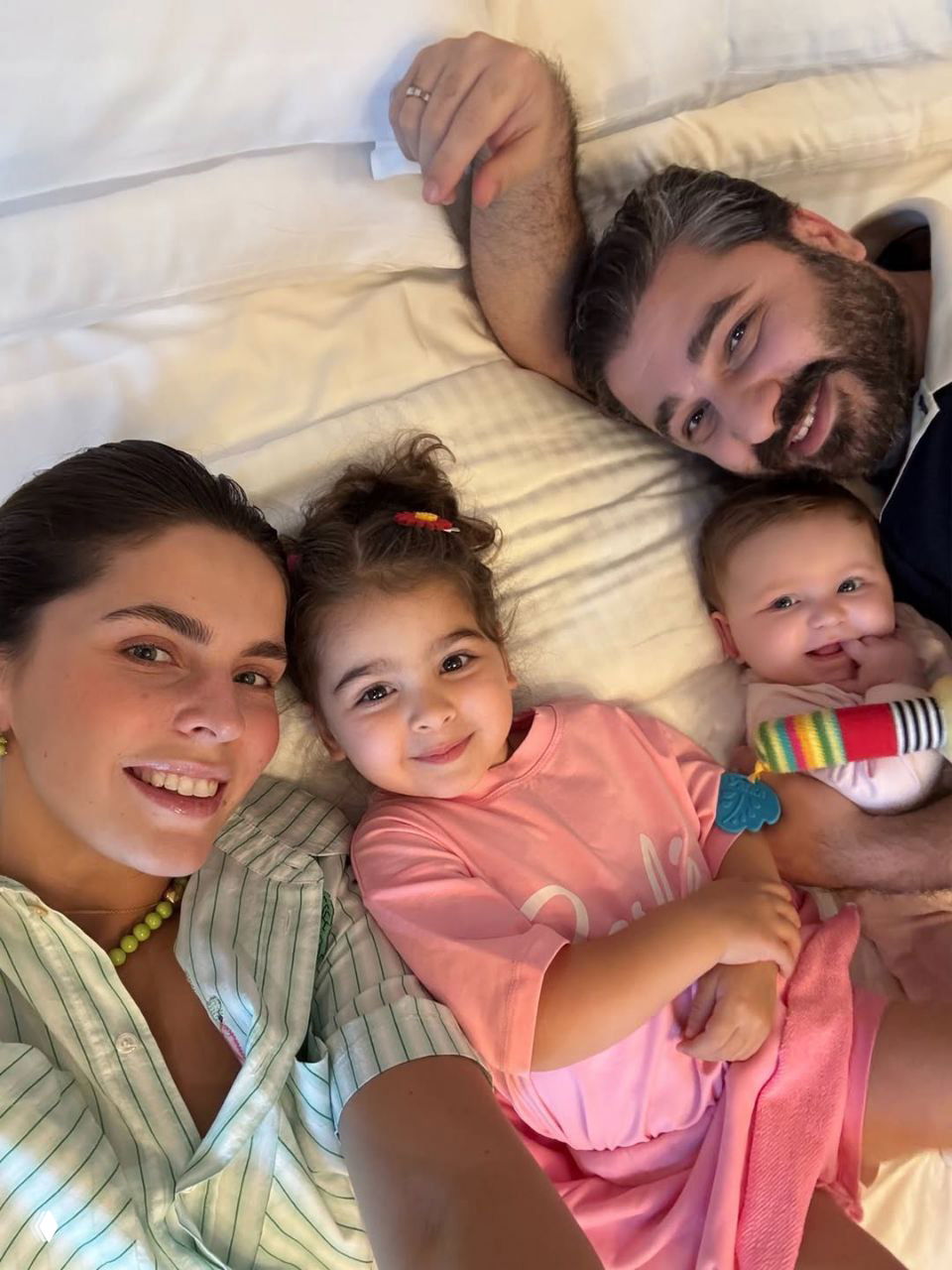 Лиза Моряк и Сарик Андреасян с дочерьми Элизабет и Шарлиз на кровати: улыбающиеся родители и дети в тёплой домашней атмосфере.