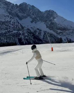 Кадр Роузи, катающейся на лыжах по подготовленной трассе: след от лыж на снегу и солнечная подсветка гор создают динамичный зимний снимок.