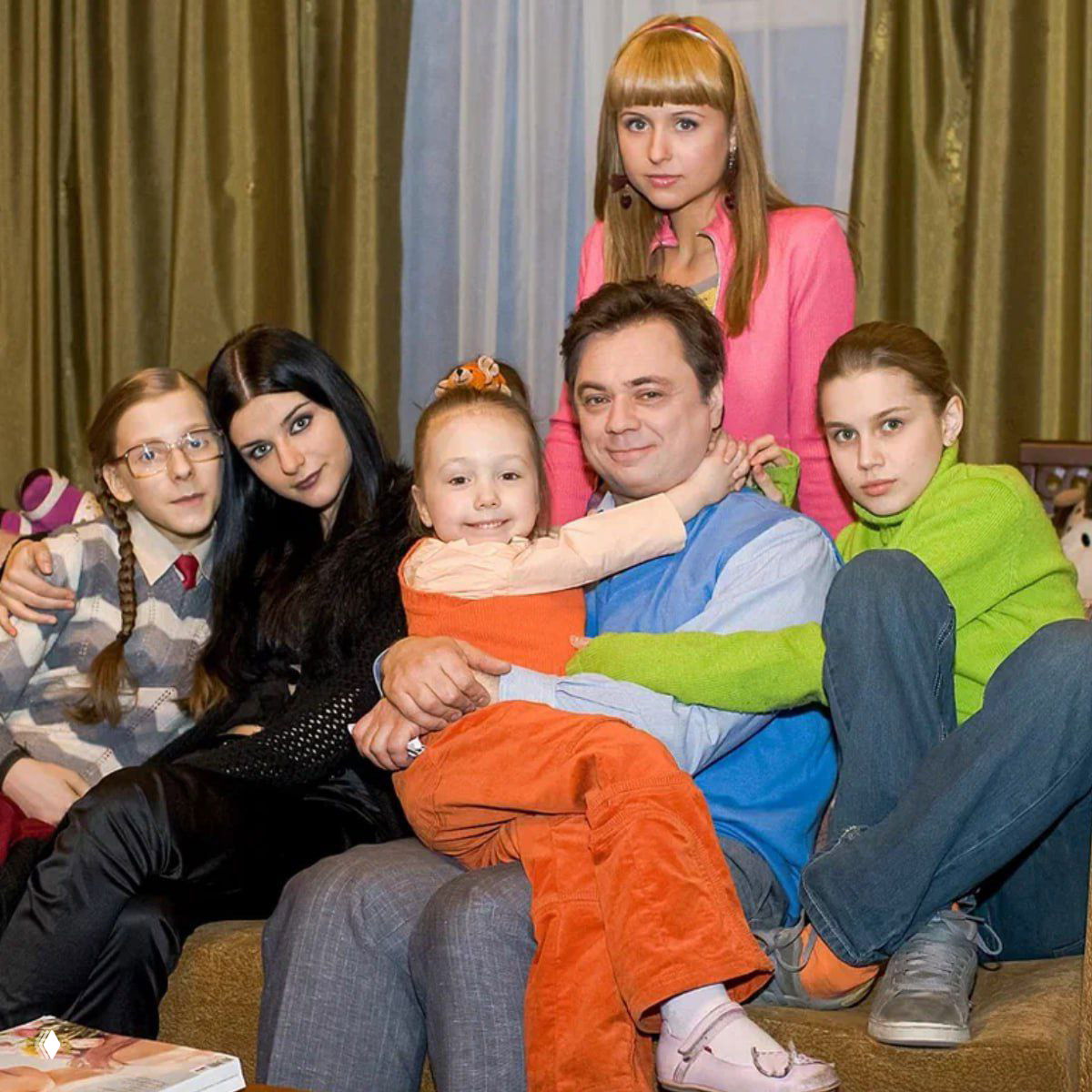 Групповое фото экранной семьи из «Папиных дочек»: актёры вместе на диване, маленькая девочка в оранжевом сидит на коленях у мужчины, студийный кадр.