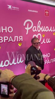 Дмитрий Дибров улыбается на фоне розового баннера премьеры: люди и зрители снимают его на телефоны, на заднике видны логотипы.