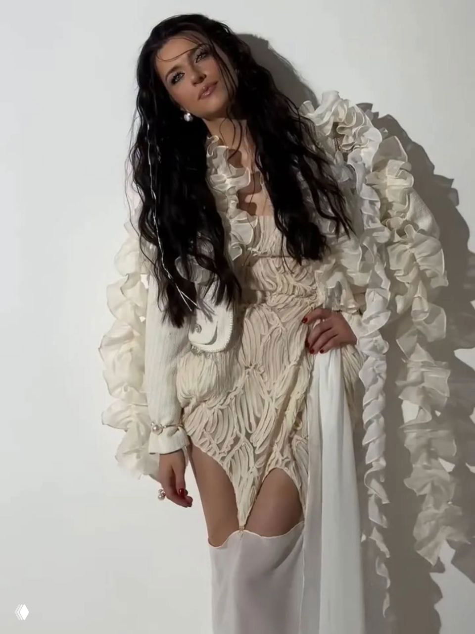 Женщина в светлом наряде с развевающимися тканями позирует перед белым фоном — художественная студийная фотография.