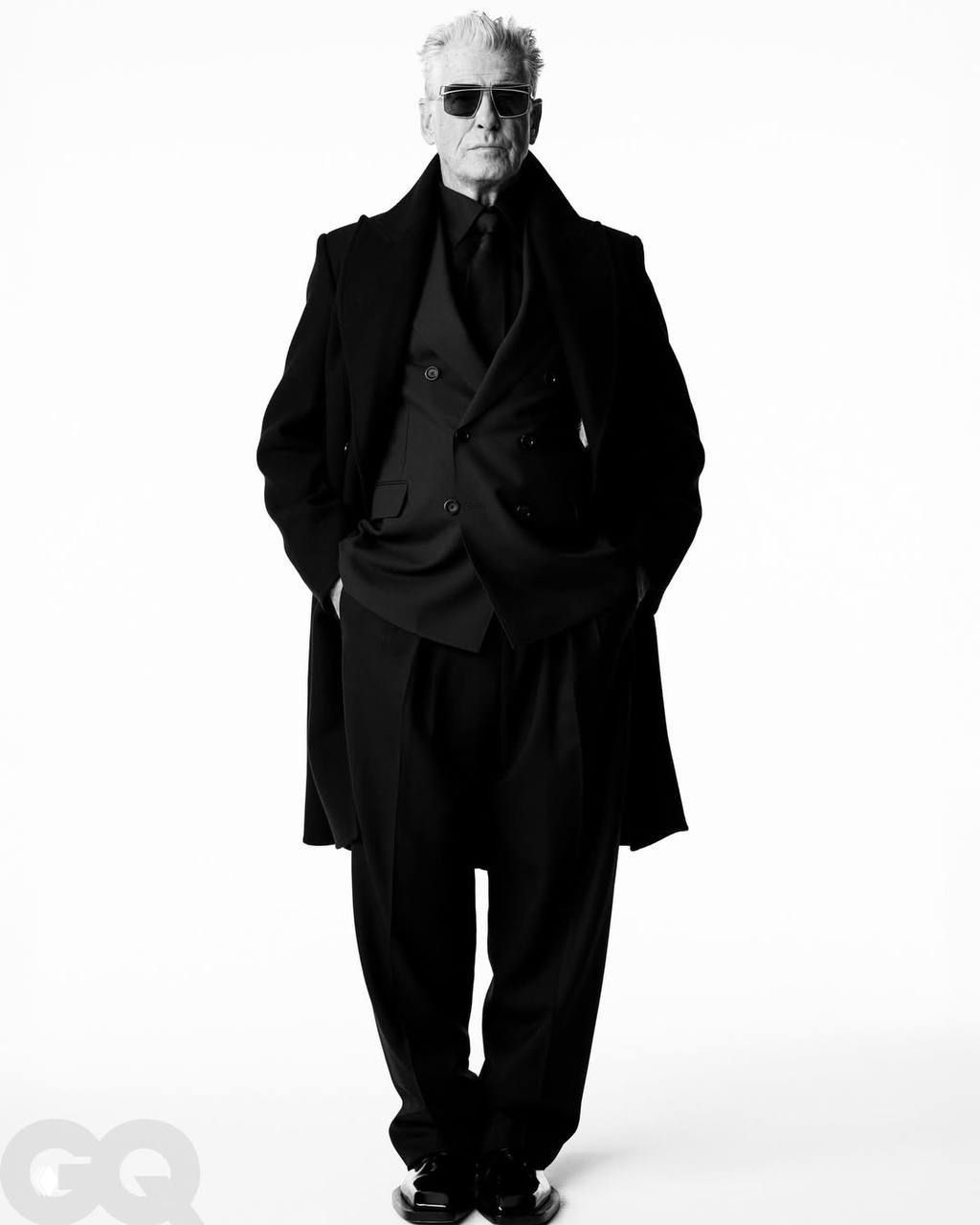 Фотосессия в чёрно‑белых тонах: полноформатный кадр мужчины в классическом пальто и костюме на белом фоне, сдержанная мужская эстетика.