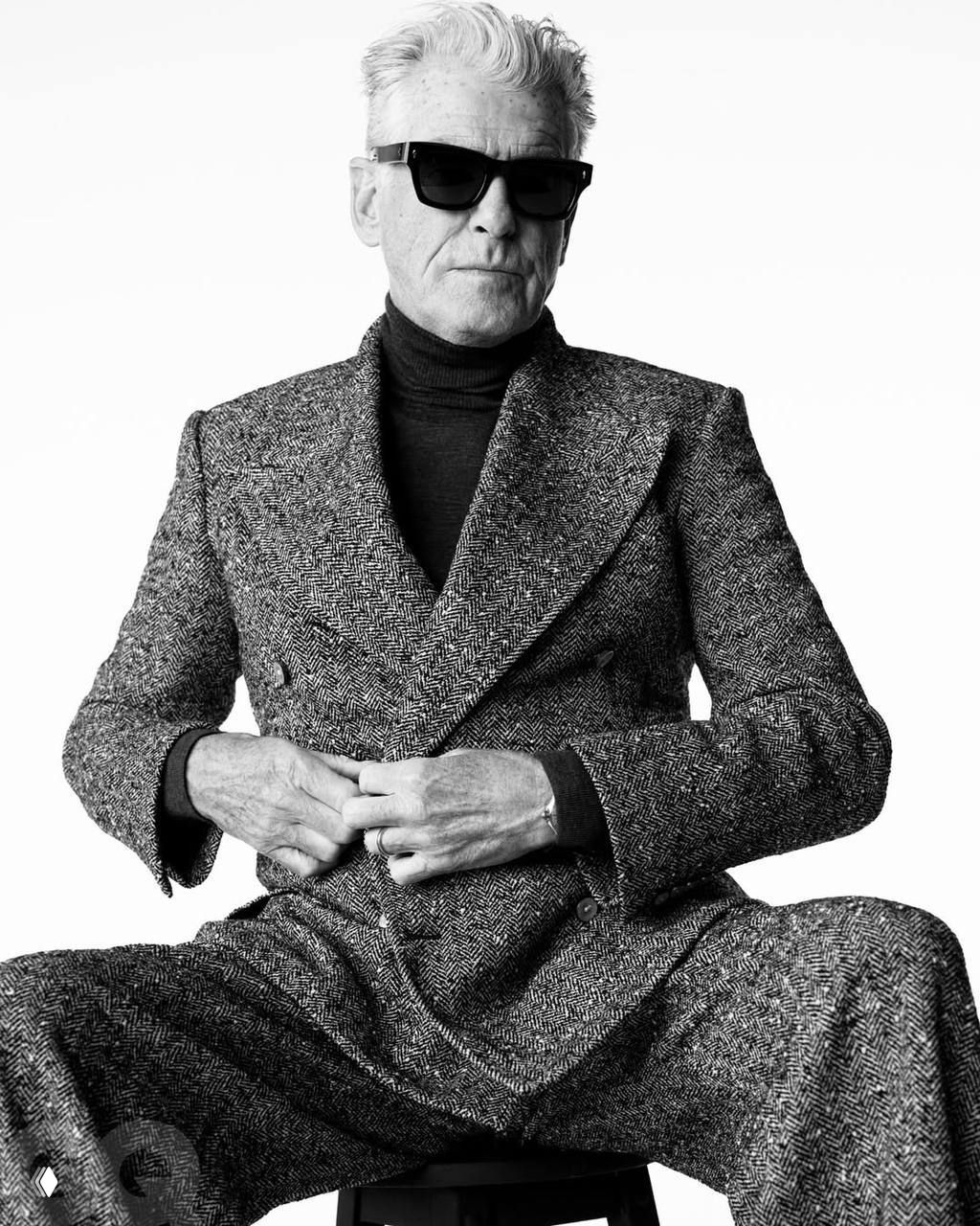 Сидячий чёрно‑белый портрет мужчины в твидовом костюме и солнцезащитных очках, акцент на текстуре ткани и уверенной позе в студии.
