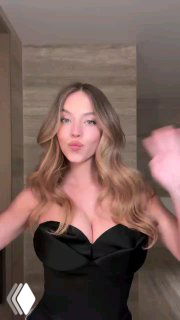 Кадр видеоролика: девушка в чёрном платье с волнистыми волосами и мягким естественным макияжем на нейтральном фоне, демонстрация образа.