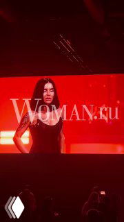 Фото с концерта «Тату» в Москве: сцена в красном свете, крупный план солистки на фоне экрана и логотип Woman.ru над сценой, публика внизу