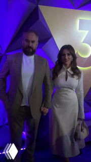 Анфиса Чехова и её жених Александр Златопольский стоят вместе на презентации нового сезона канала «ТВ-3», держатся за руки на фоне логотипа и фиолетовой подсветки.