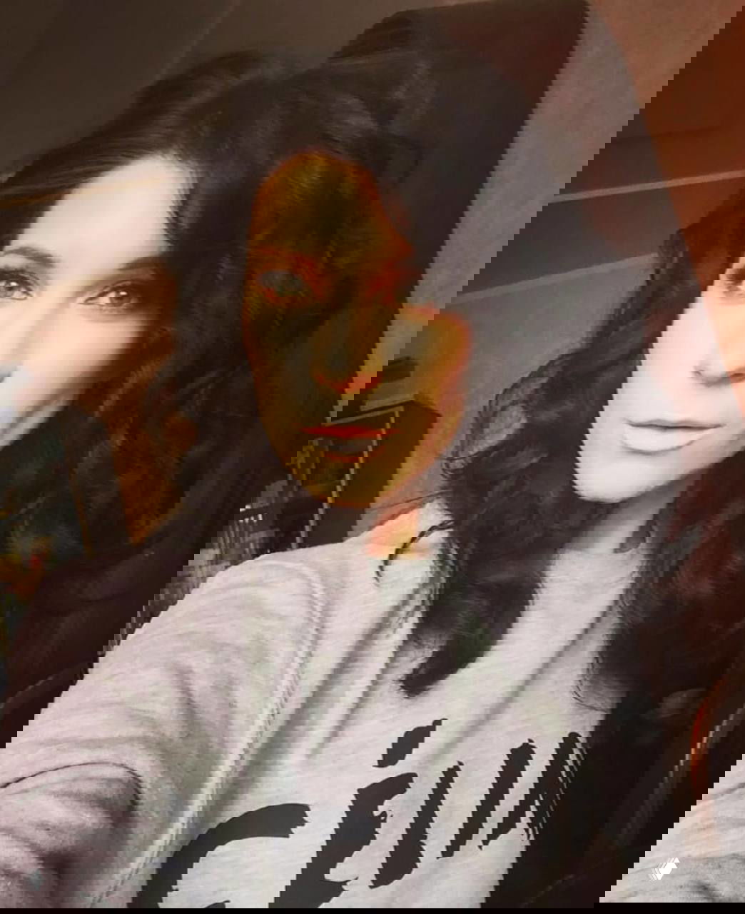 Портрет женщины с тёмными вьющимися волосами в комнатной обстановке, выражение лица спокойное, акцент на лице и причёске.