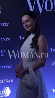 Женщина в светлом платье позирует на фоне баннера Woman.ru на вечеринке Celebrity Party в пространстве Kiki Event Dom.