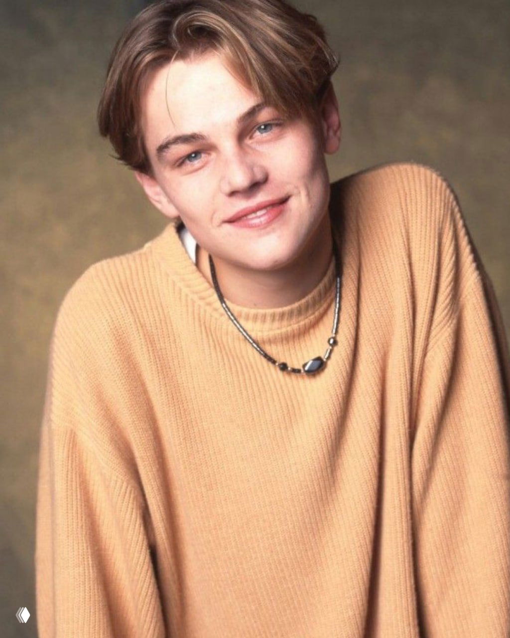 Молодой Леонардо ДиКаприо в светлом свитере на раннем портретном снимке, мягкая улыбка и юношеский образ из начала карьеры.