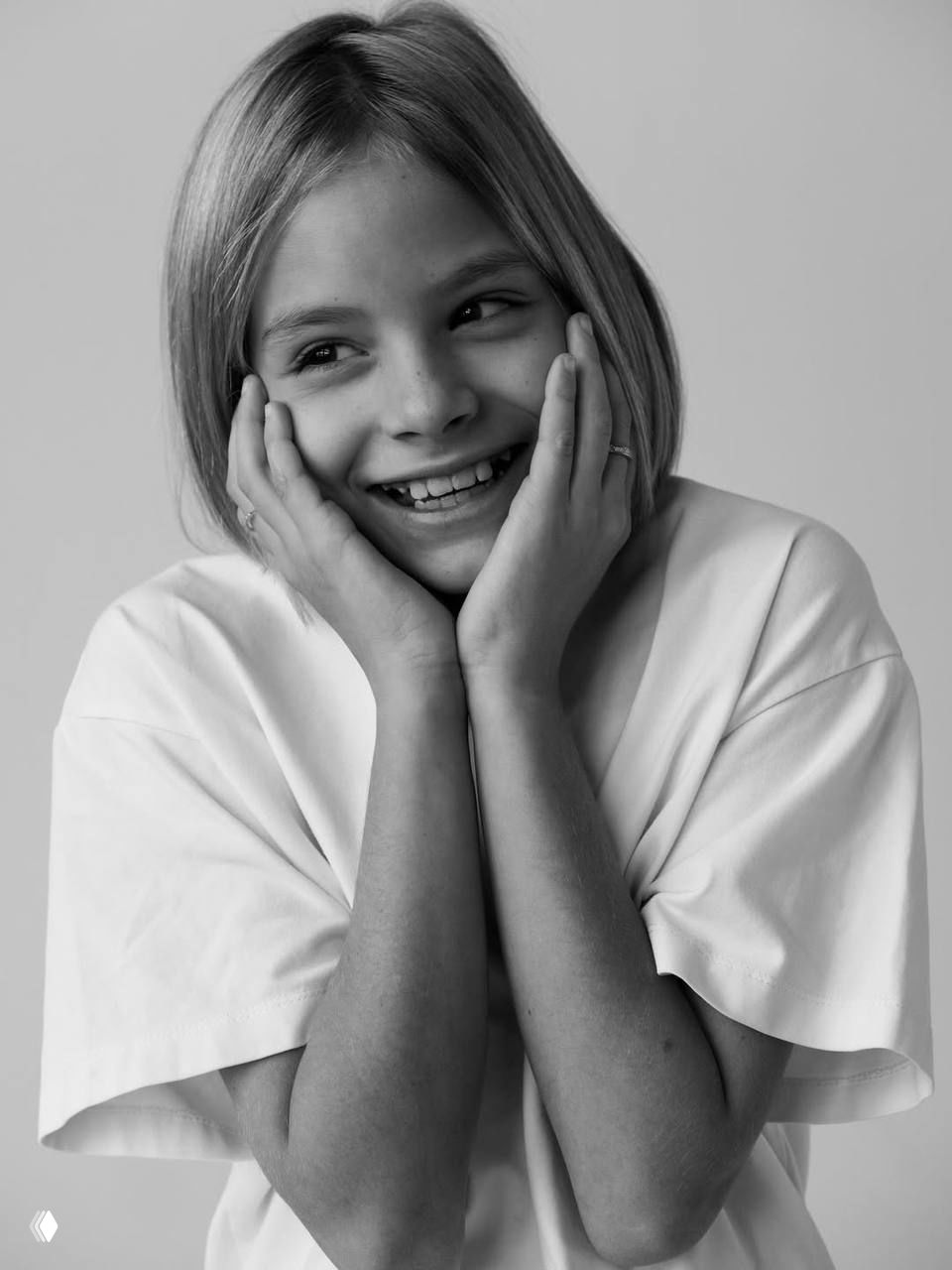 Чёрно‑белый крупный портрет девочки, студийный фон, нейтральное выражение лица, естественный свет и минималистичный кадр.