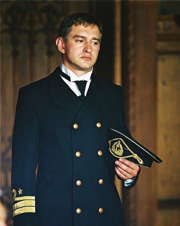 Мужчина в форме морского офицера с документом в руках, официальный костюмный образ, театральная или кинематографическая сцена.