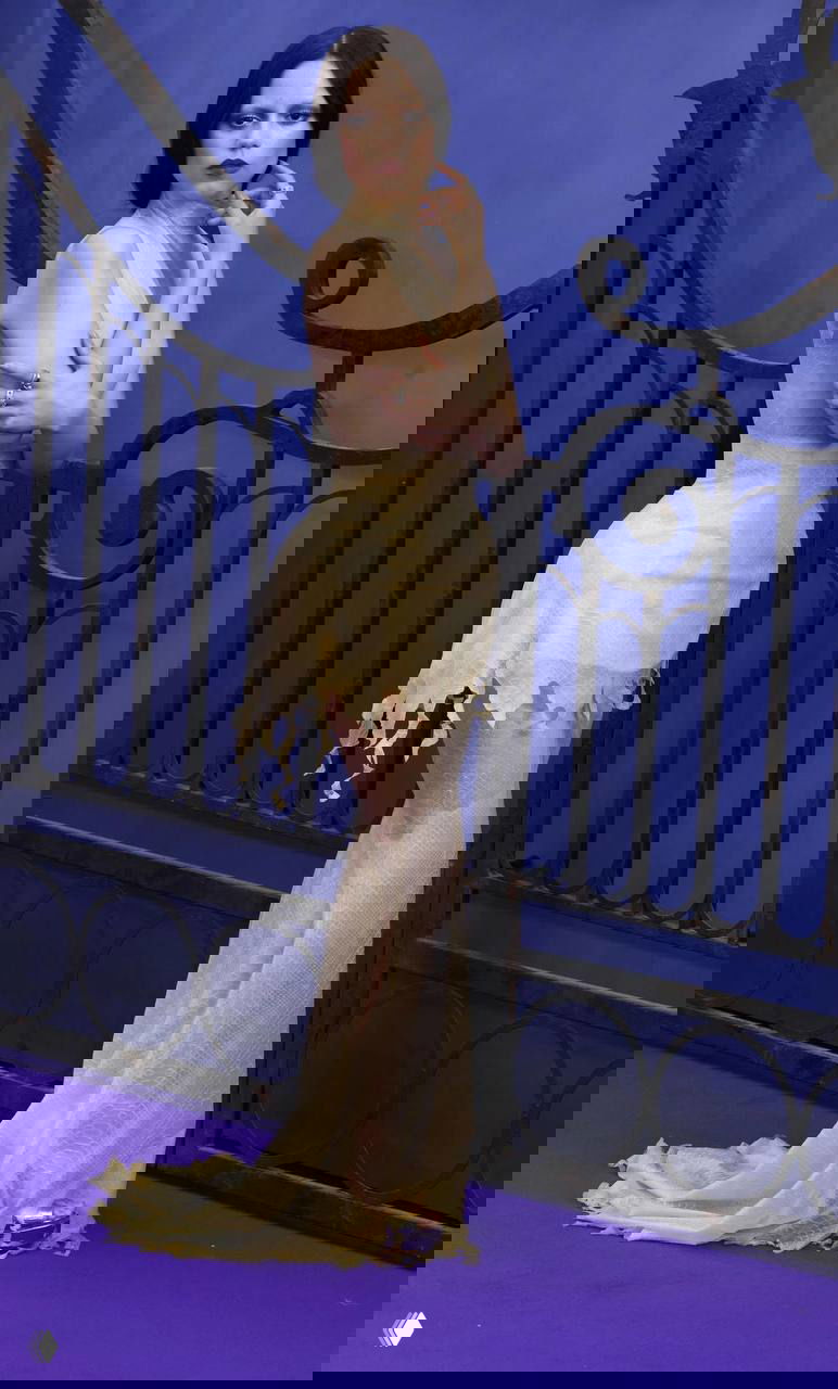 Кремовое полупрозрачное платье с потертыми краями и лёгким шлейфом, тонкий силуэт и драматическая постановка на фоне декоративной ограды