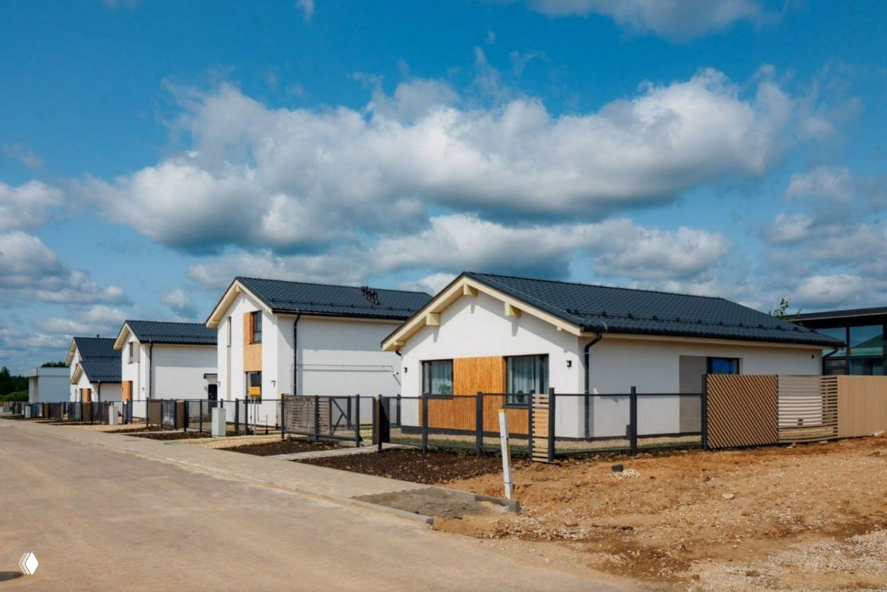 Ряд одноэтажных компактных домов в новой застройке: одинаковые фасады, ограждения участков и подготовленные дороги в поселке.