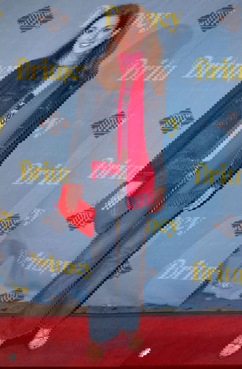 Энн Хэтэуэй в джинсовом костюме с ярким розовым шарфом и красным клатчем на красной дорожке в молодые годы; кэжуал-вдохновлённый образ.