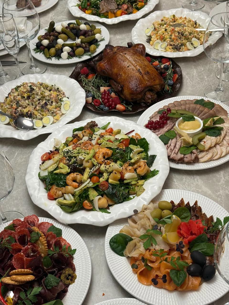 Фотография праздничного стола с салатами, запечённой птицей и разнообразными закусками на белых сервировочных тарелках — семейный новогодний стол.