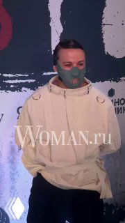 Никита Кологривый в светлом худи и защитной маске позирует на фоне баннера на премьере третьего сезона сериала «Метод», виден логотип Woman.ru на изображении.