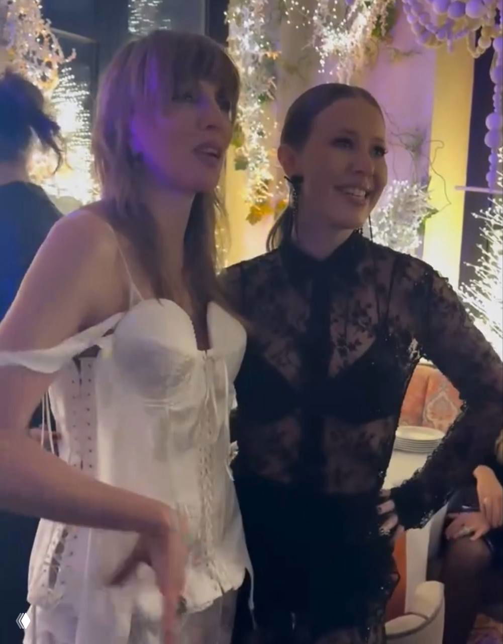 Две женщины в вечерних нарядах общаются на фоне сверкающих украшений и праздничного освещения в интерьере ресторана