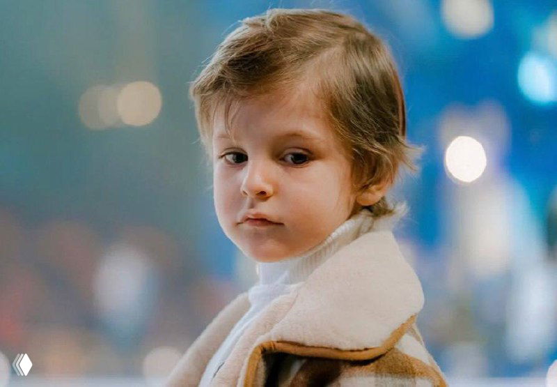 Портрет ребёнка в светлой дублёнке на фоне размытого праздничного освещения — задумчивое выражение лица во время представления.