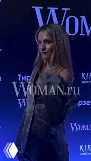 Женщина в серебристом наряде на фоне фиолетового баннера Woman.ru; фото сделано на вечеринке Celebrity Party в Kiki Event Dom.