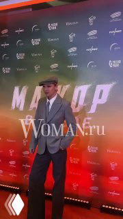 Мужчина в светлом костюме и кепке стоит на фоне бренд-стены с названием фильма, фотозона премьеры выполнена в тёплых тонах.