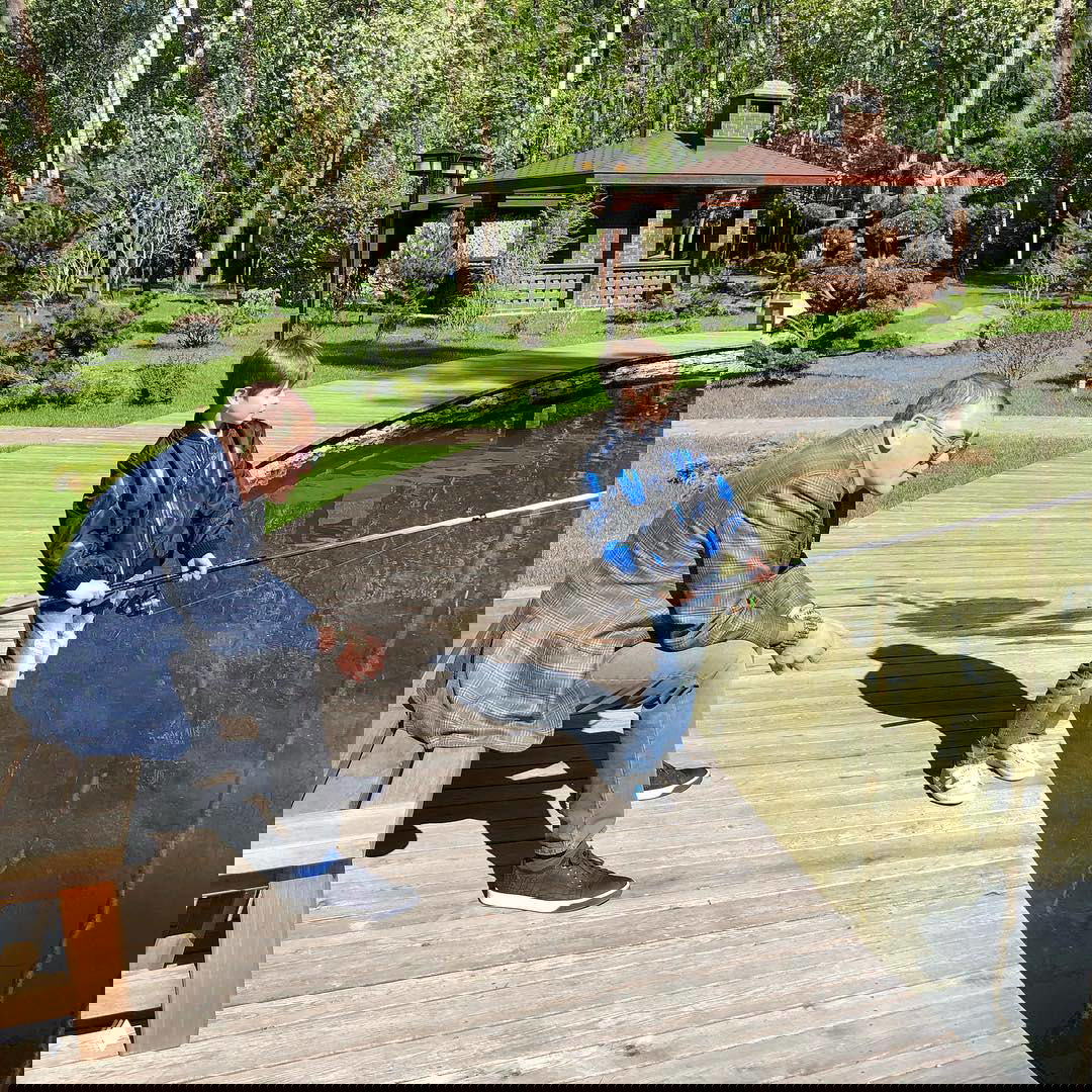 Деревянная пристань у пруда на территории усадьбы: мужчина и ребёнок с удочкой на фоне зелёного парка, семейная сцена на участке продаваемого дома.