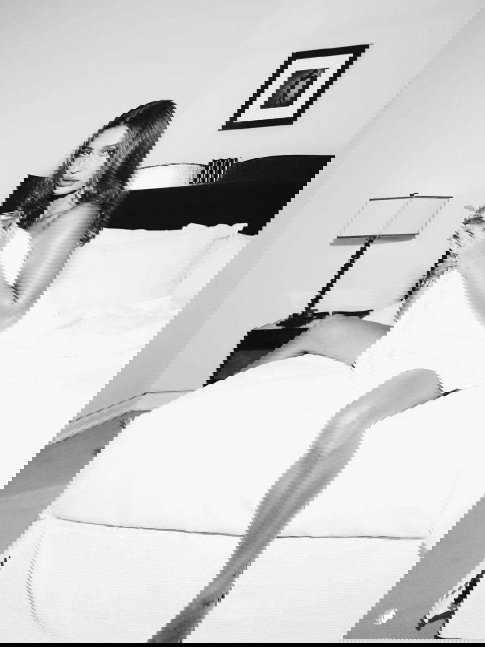 Чёрно‑белый кадр в спальне: модель сидит на кровати, завернутая в простыню, гламурная ретро‑эстетика фотосессии