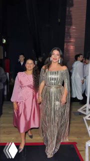 Женщина в элегантном платье шагает по красной дорожке с дочерью в розовом наряде: вечернее мероприятие, праздничный выход в свет.