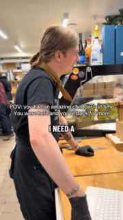 Продавец у прилавка в процессе нарезки сыра: рабочая атмосфера, инструменты для разделки и витрины с продуктами.