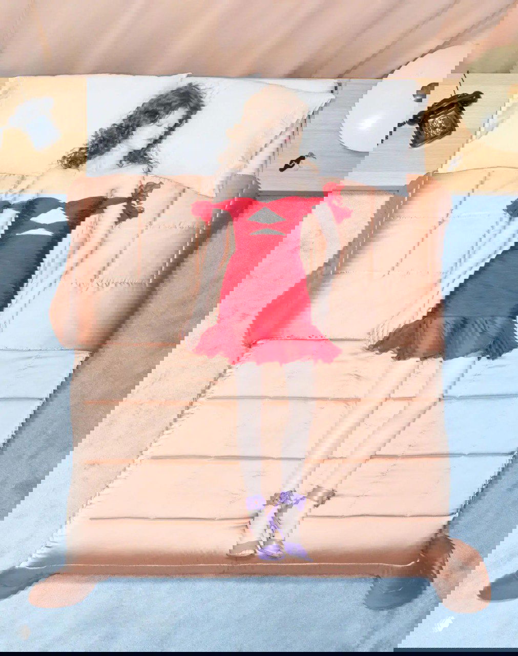 Кадр сверху: модель в красном платье Valentino лежит на кровати — стилизованная рекламная съёмка круизной коллекции.