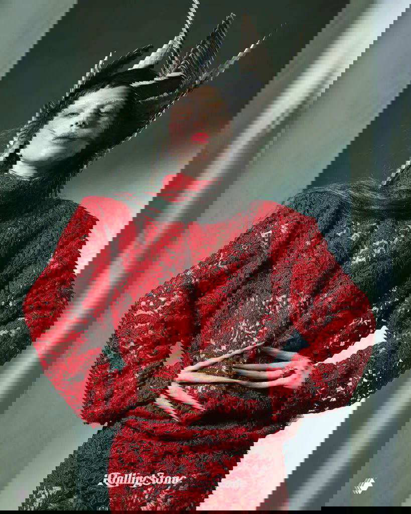 Крупный портрет женщины в красном кружевном наряде с декоративными рогами и удлинёнными пальцами — художественный fashion-кадр.