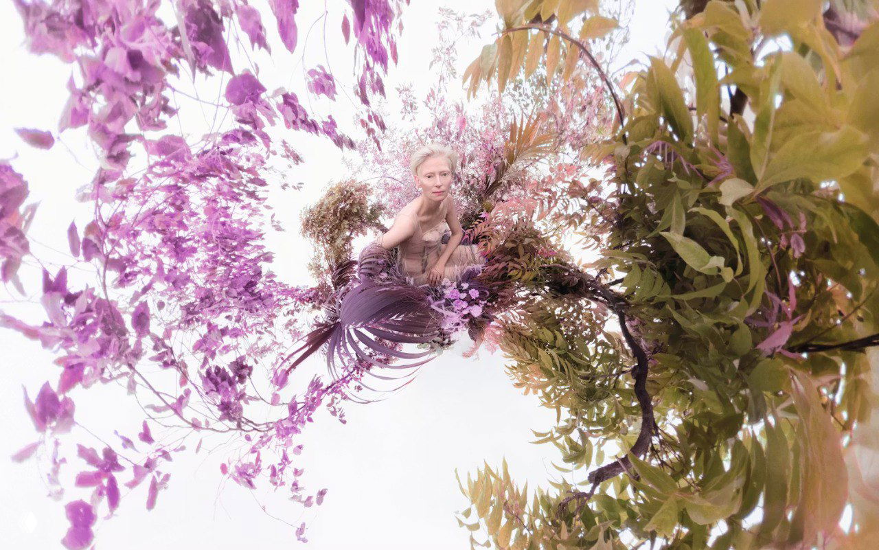 Сюрреалистичная композиция с цветущими ветвями и моделью в центре, пастельные тона и растительные элементы создают ощущение сада и природы.