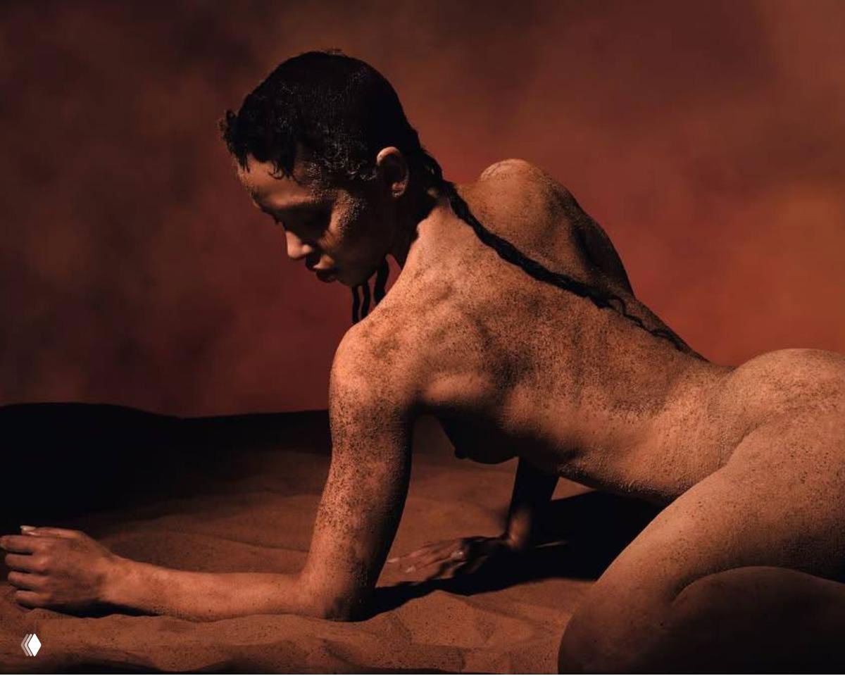 Портрет модели на тёплом коричнево‑песочном фоне, кожа и поза акцентируют природную текстуру земли и минималистическую эстетику стихий.