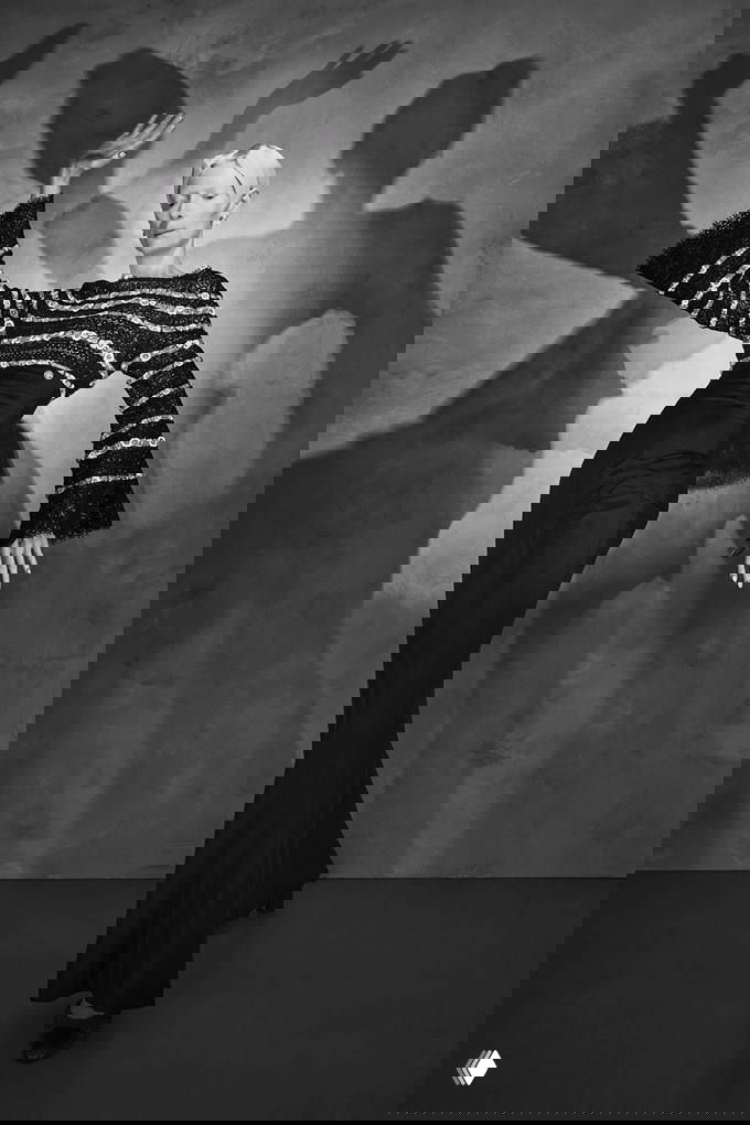 Чёрно‑белое студийное фото модели в длинном облегающем платье и полосатом топе от Chanel; драматичные тени создают театральный фон.