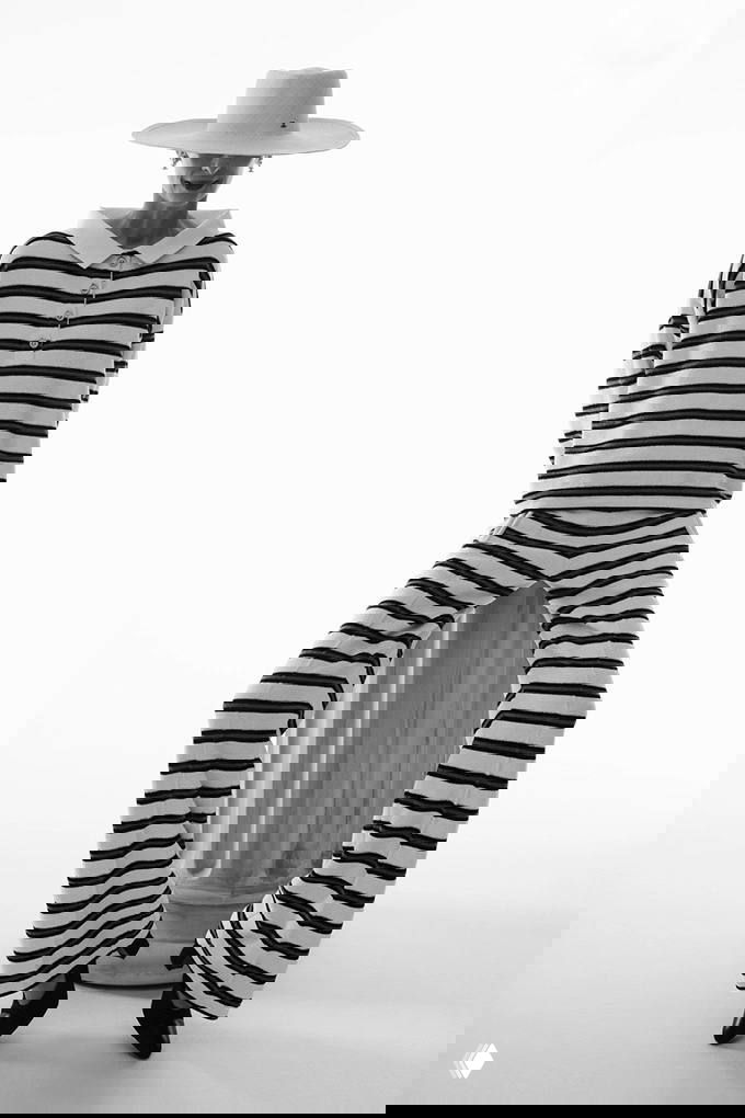 Модель в широком полосатом костюме и шляпе в студийной съёмке; крупные горизонтальные полосы и контрастный свет подчёркивают силуэт.