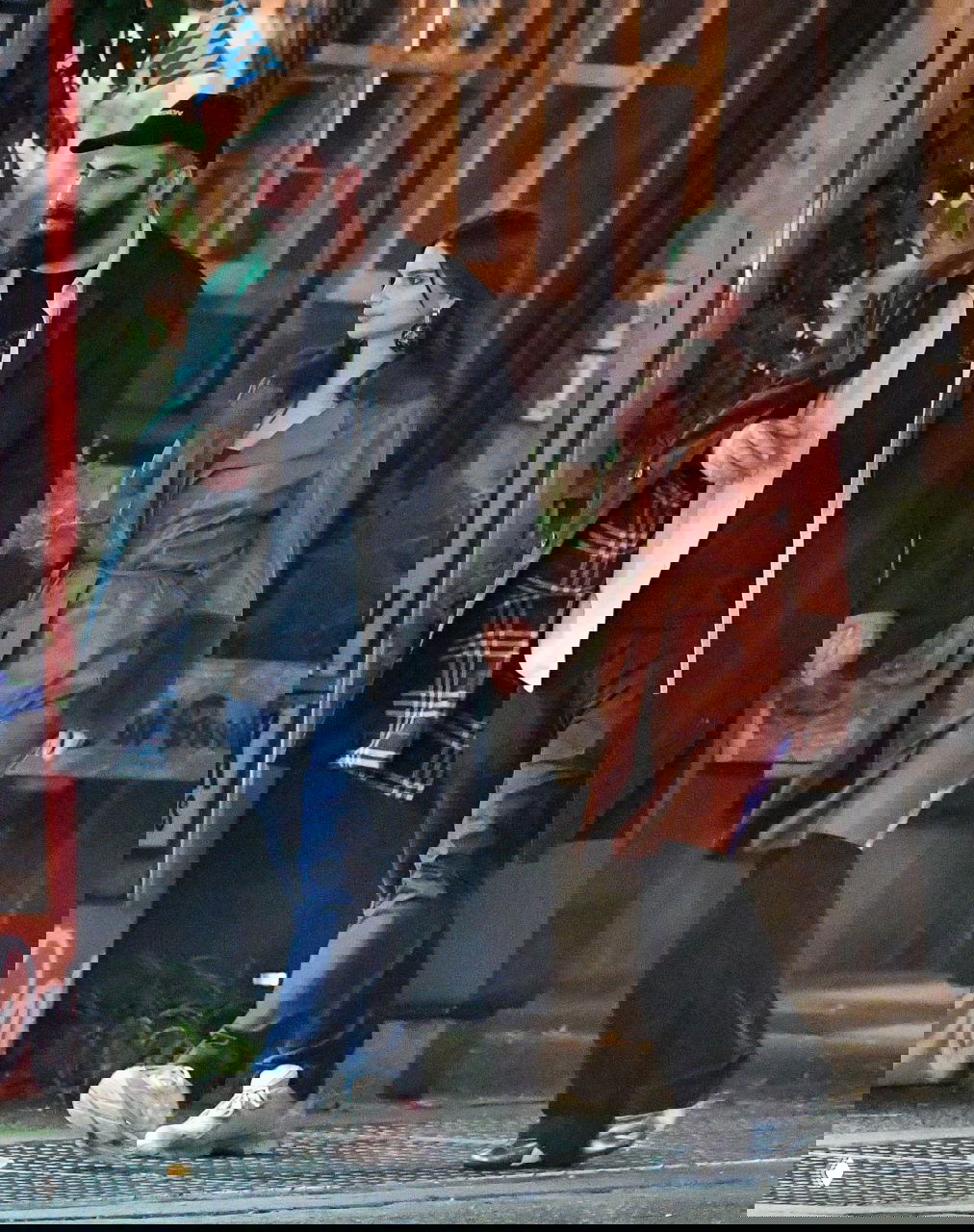 Эмили Ратаковски держит за руку мужчину в кепке — парочка идёт по тротуару в тёплых пальто, кадр папарацци на городской улице вечером