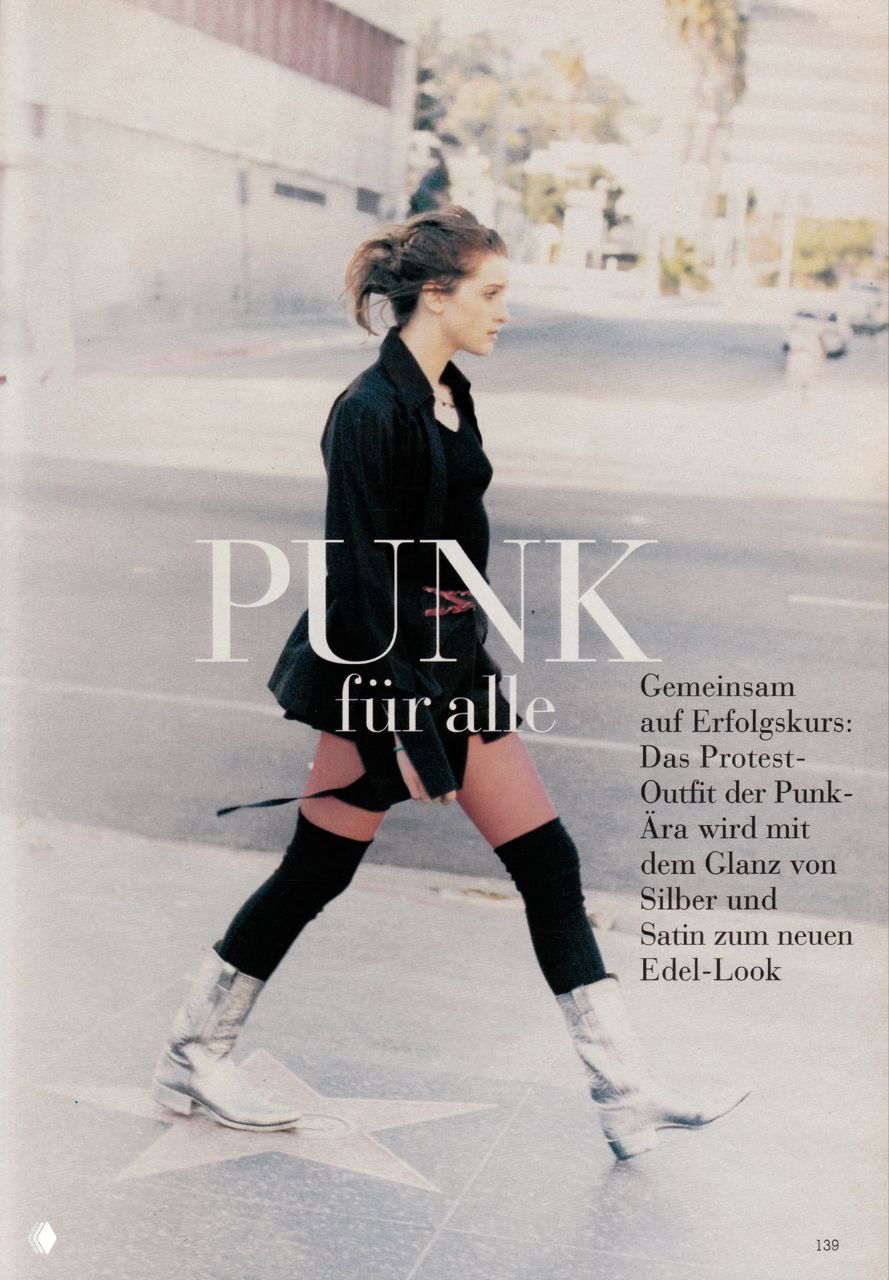 Архивный кадр 1994 года: молодая женщина в лёгком панк‑стиле идёт по улице в серебристых казаках, мини‑юбке и свободном пиджаке на фоне города.