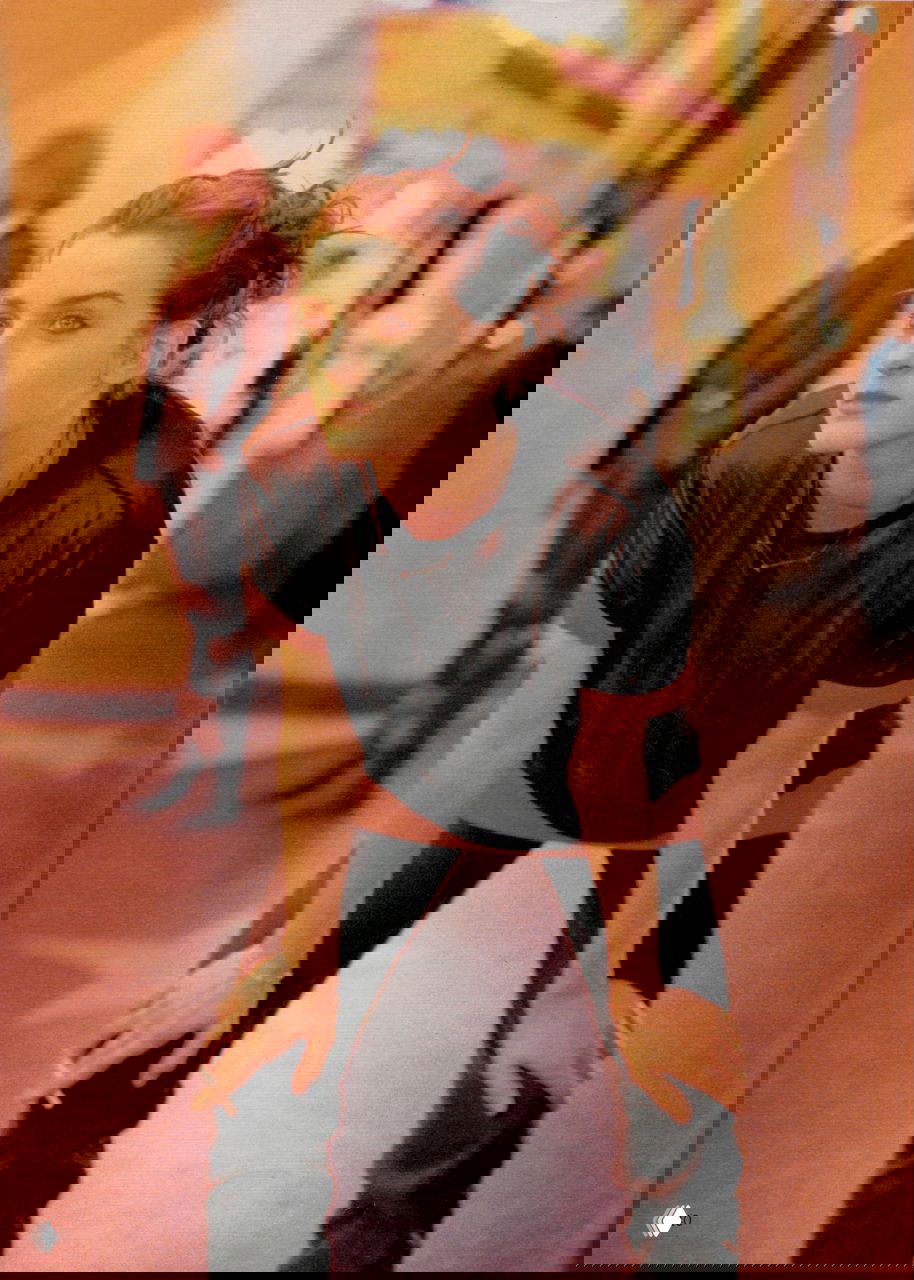 Портретный кадр из модной съёмки: модель в тёплом оранжевом свете, расслабленная поза, выразительный взгляд и неформальный стиль одежды в винтажной палитре.