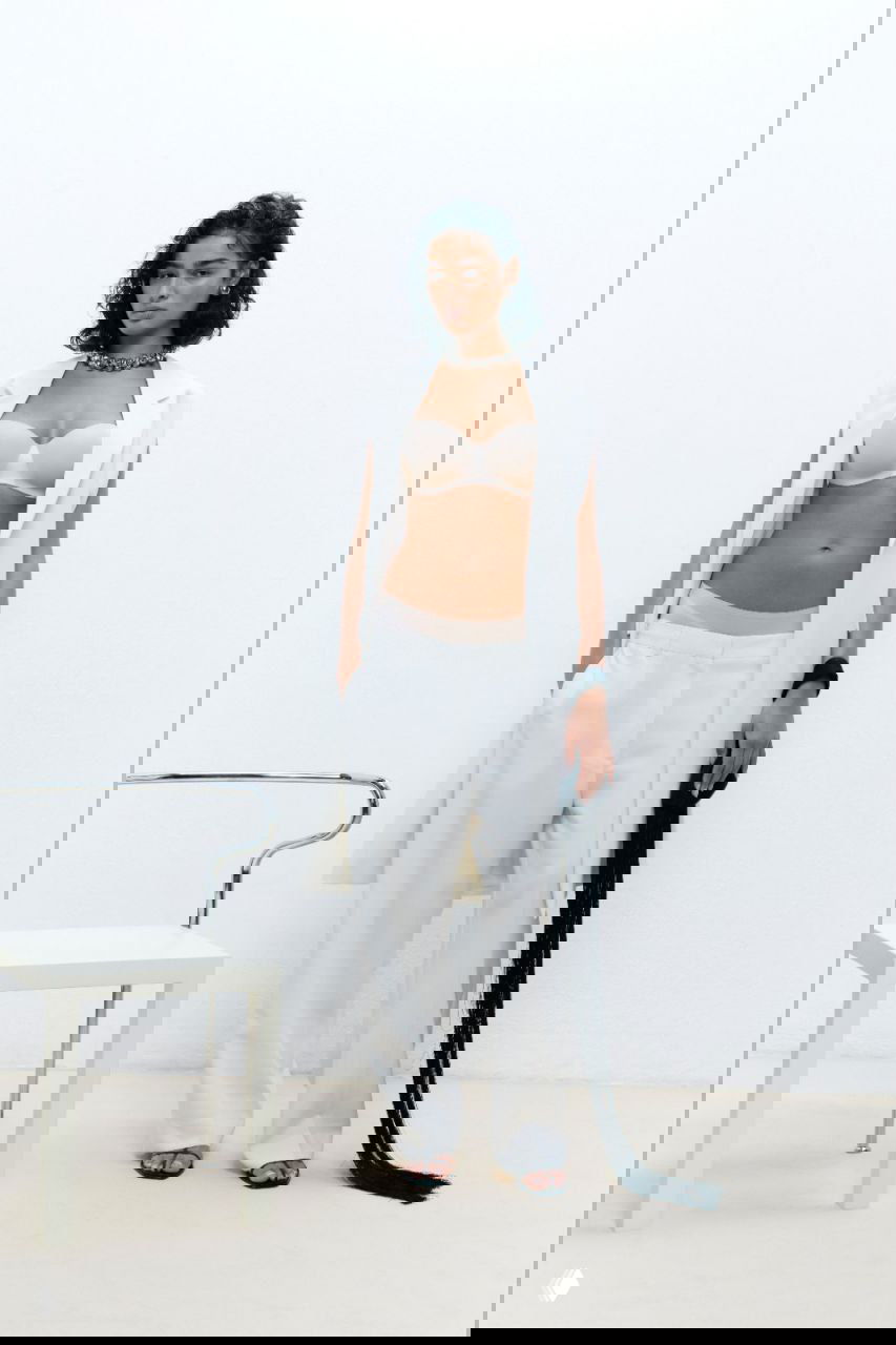 Фотосъёмка модели в бежевом бюстгальтере и белых брюках в минималистичной студии — реклама коллекции белья Chantelle.