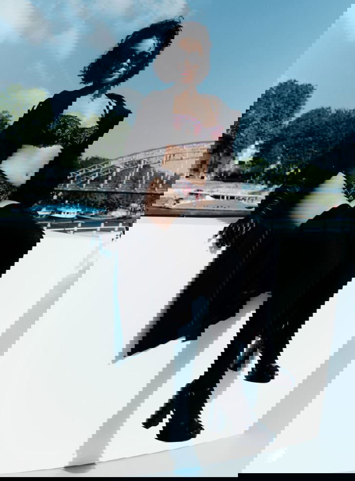 Модель в чёрном кружевном комплекте сидит на борту лодки на фоне реки и мостов — образ из кампании Chantelle в Париже.