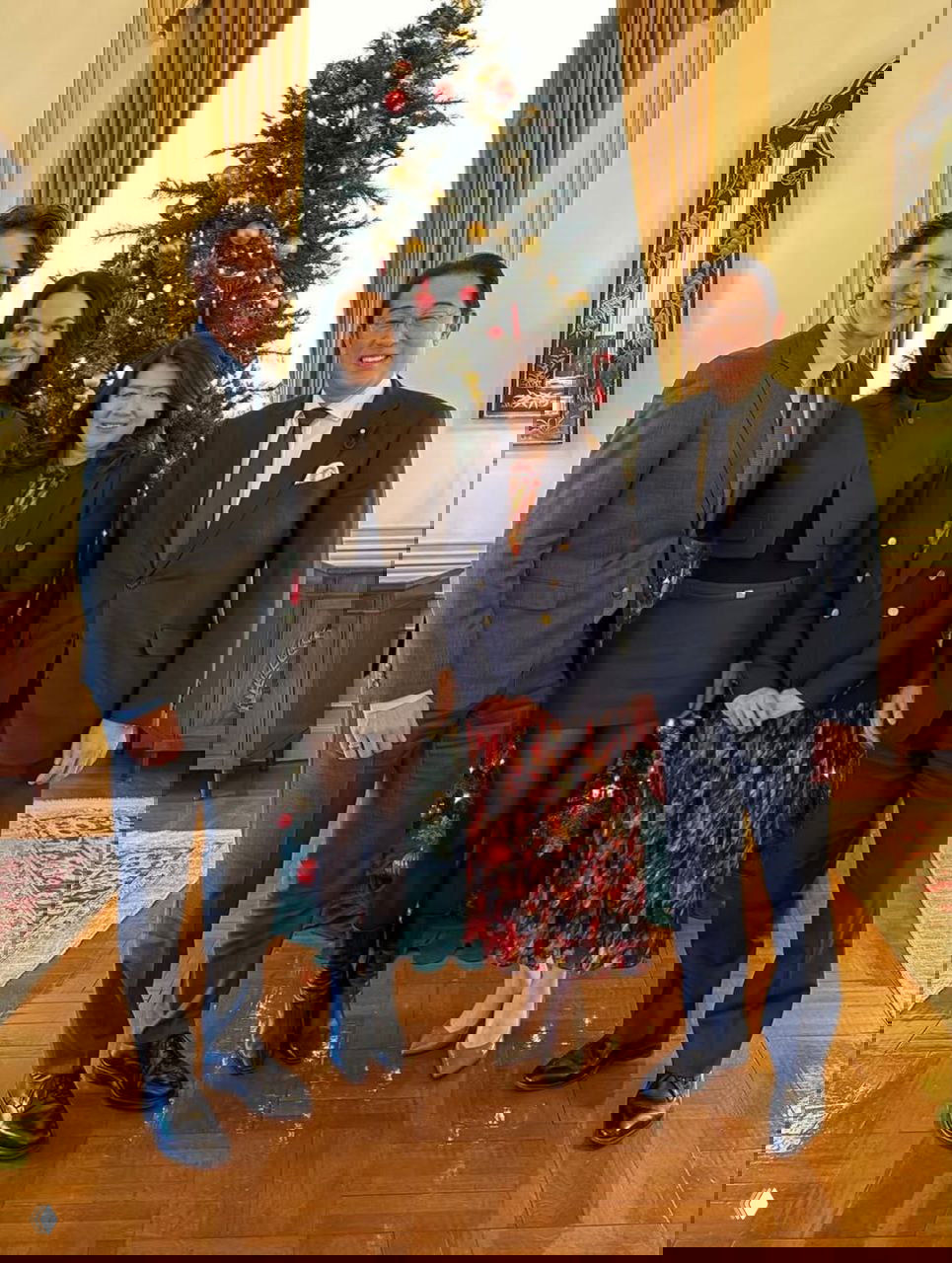 Четверо человек позируют у украшенной рождественской ёлки в торжественном кабинете — праздничная встреча в Токио.