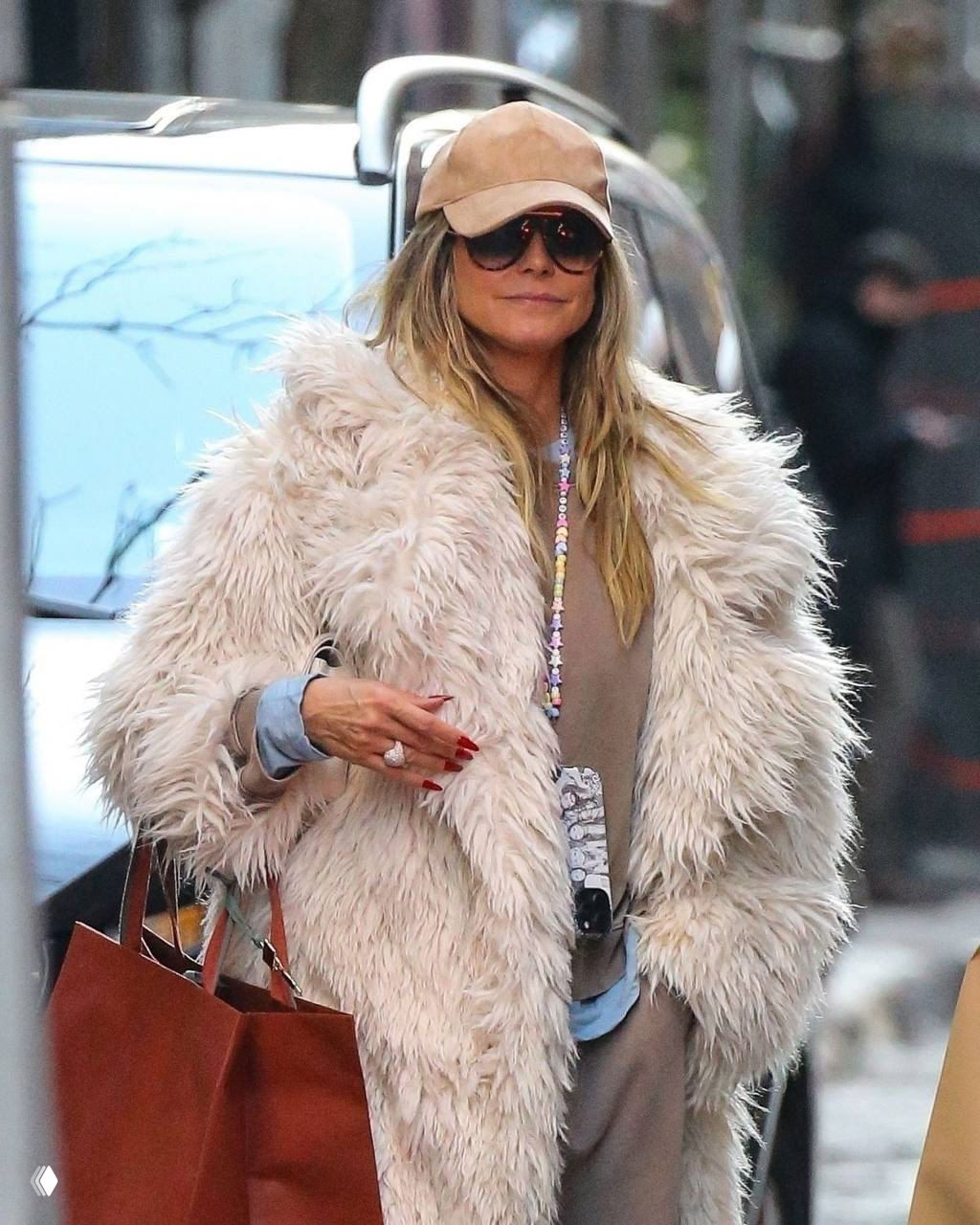 Женщина в объёмной меховой шубе светлого оттенка и бейсболке, крупный аксессуар и солнцезащитные очки в городском образе.