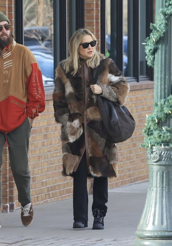 Женщина в длинной мозаичной шубе тёмных и светлых оттенков, тёмные брюки и солнечные очки — эффектный уличный образ.