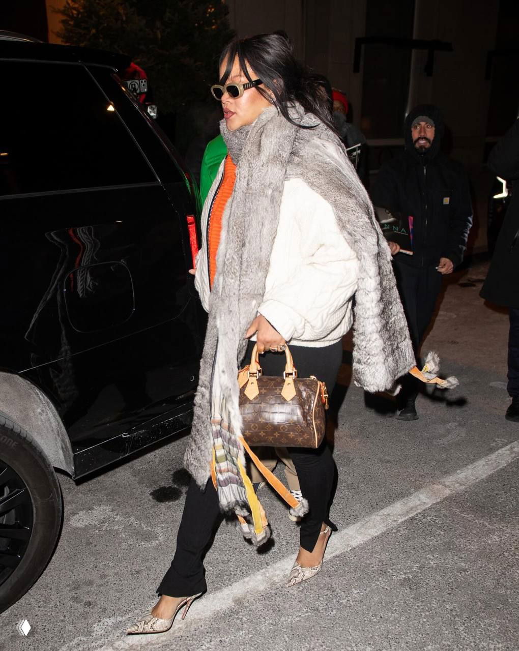 Уличное фото: женщина в объёмном меховом шарфе и крупной сумкой спешит мимо автомобиля, контраст текстур и аксессуаров.