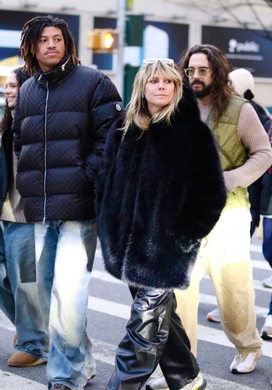 Группа людей на городской улице, одна фигура в тёмной объёмной шубе и кожаных брюках — контрастный уличный образ в толпе.