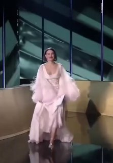 Полный рост: Милли Бобби Браун в нежно-розовом платье Tamara Ralph и белой накидке с меховой отделкой идёт по сцене премии, общий план.