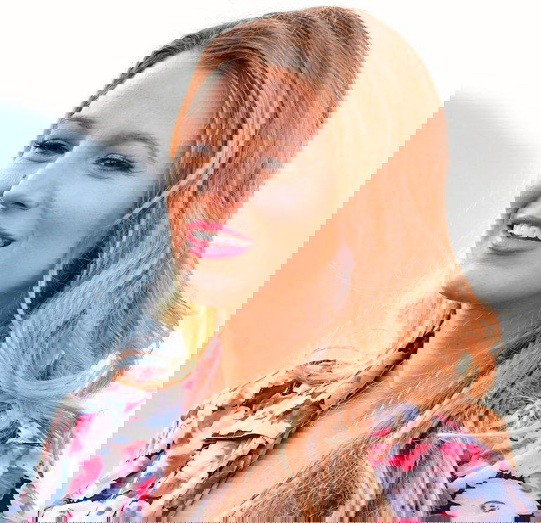 Улыбающаяся женщина со светлыми волнистыми волосами и лёгким макияжем на светлом фоне — пример естественной укладки без фена.